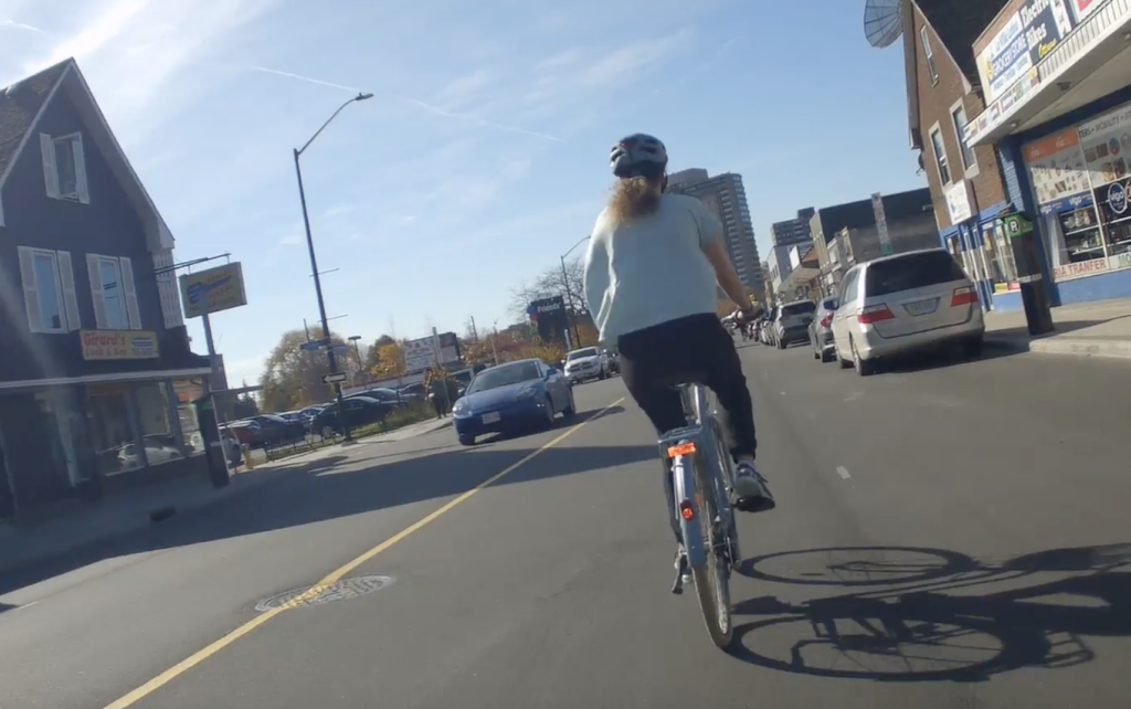 Picture of a person riding their bicycle on Montreal Road north to Cummings bridge, "sharing" the road with motorists and a door zone.