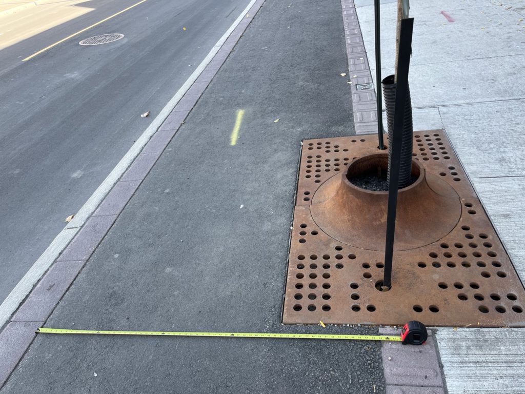 Picture shows measuring tape on cycle track showing space between where the tree grate ends and the cycle track exists.
