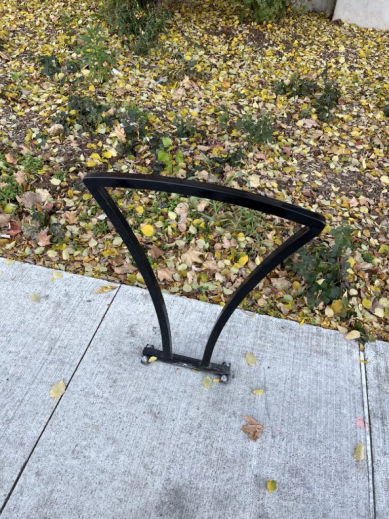 Bicycle parking rack is brown and triangular. Image shows the bolts for the rack are drilled into the sidewalk