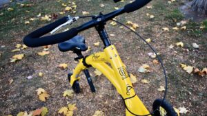 Picture of a yellow walking bicycle outside on the grass covered with scattered yellow leaves
