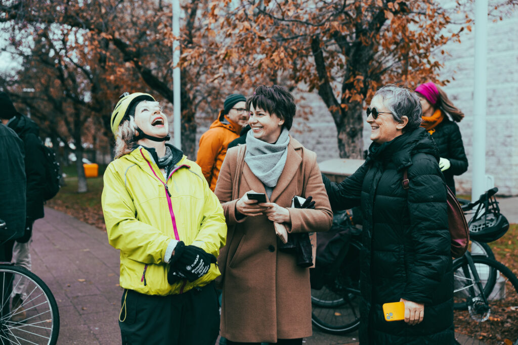 Two of the speakers and a councillor laughing together at the Bill 60 rally. People and bikes can be seen in the background.