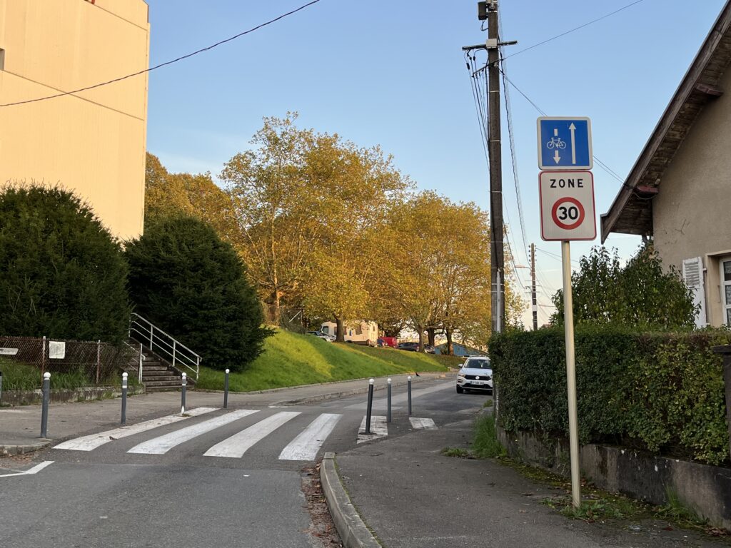 A 30 kph zone sign on a narrow one-way street with a sign above it showing that people on bikes can bike against traffic.
