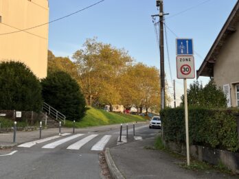 A 30 kph zone sign on a narrow one-way street with a sign above it showing that people on bikes can bike against traffic.