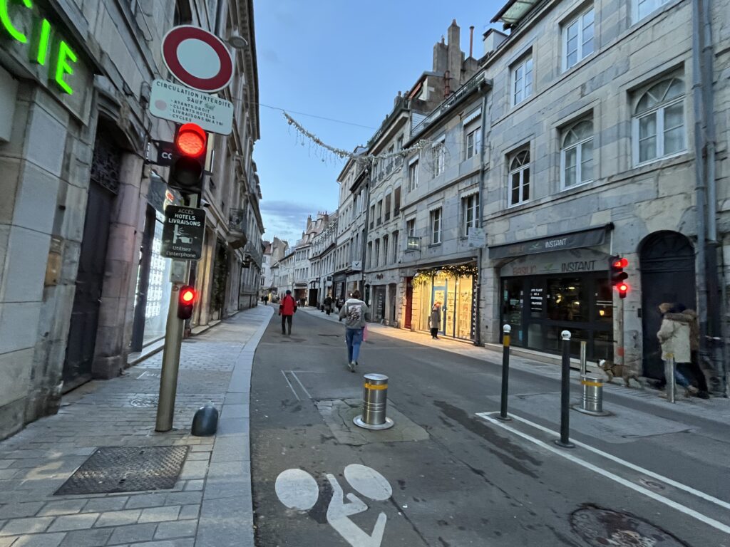 Two retractable bollards and a couple of posts blocking a street into downtown Besançon. Bollard to the right comes down upon activation by bus drivers. On the left, a sign says that delivery drivers and hotel visitors must ring in for hotels or stores to bring down the bollard and let them in.