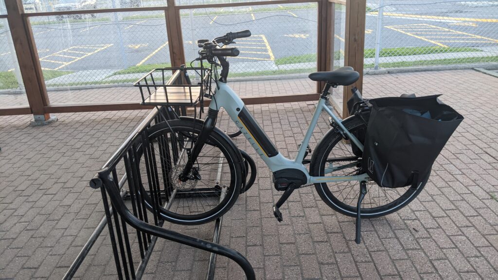 A white step through bicycle parked at a school yard style bicycle rack, the bicycle wheel is the only part able to make connection with the bicycle rack.