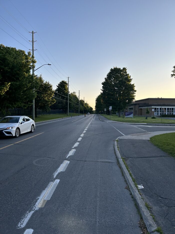 Hemlock Road near Manor Park Public School. Picture is taken from the painted bike lane and shows a car in the opposite direction and the school further up to the right.